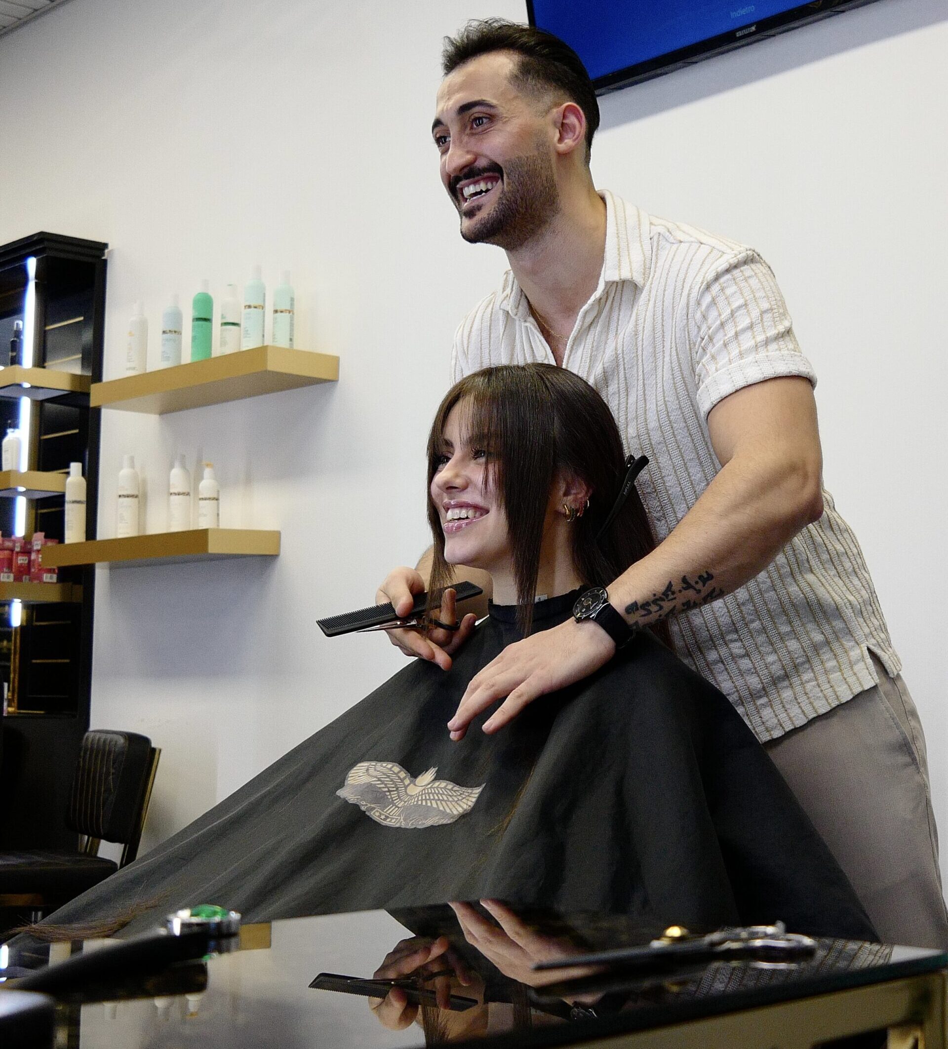 Melark sorride mentre acconcia i capelli di una cliente.